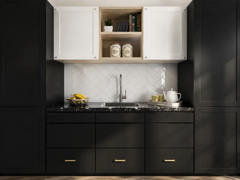 Modern black kitchen with white upper cabinets, a white herringbone tile backsplash, black marble countertop, and brass drawer pulls.