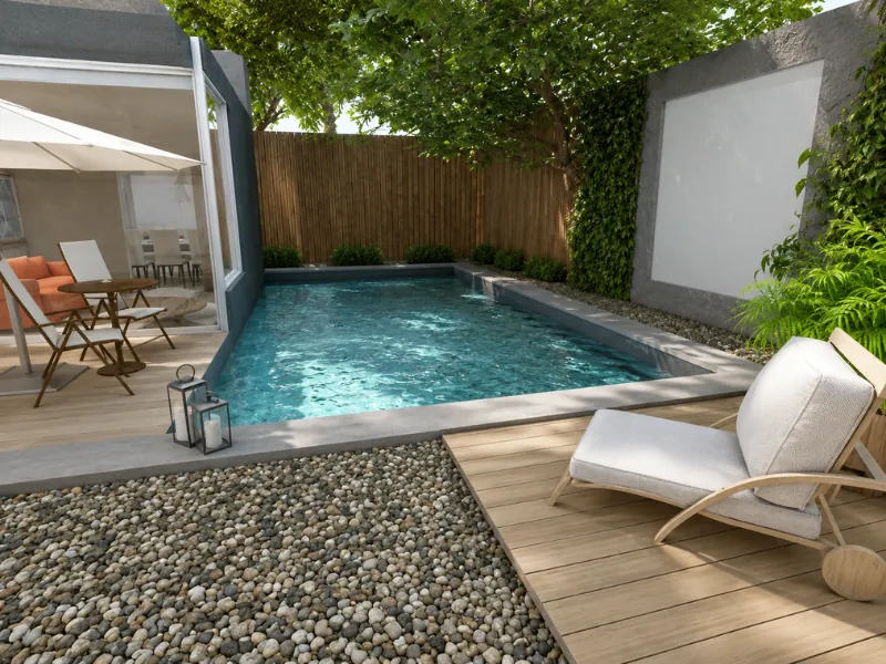 Small backyard pool with a large outdoor projection screen, wooden deck, lounge chair, and pebble landscaping.