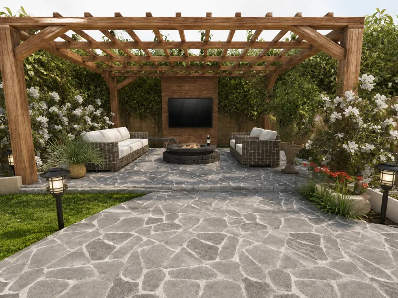 Covered backyard lounge under a wooden pergola with outdoor sofas, a fire pit, mounted TV, and stone patio.