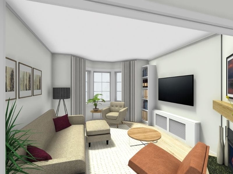 3D rendered living room with a beige sofa, matching armchair with ottoman, and an orange accent chair around a round wooden coffee table. A wall-mounted TV sits above a white console, with bookshelves on either side. Large bay windows with light curtains let in natural light, and framed artwork, plants, and a floor lamp add decorative touches.