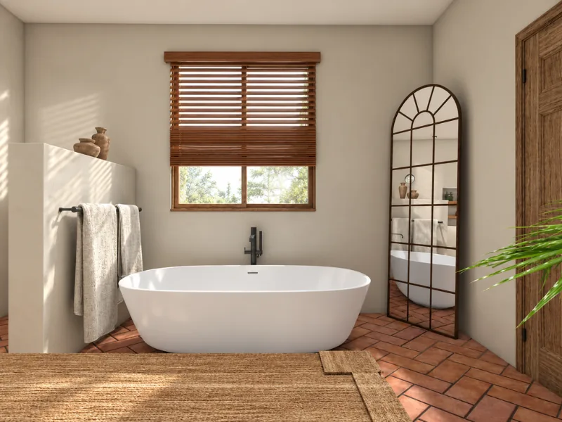 Freestanding bathtub in a Southwestern-style bathroom with terracotta tile and wood blinds.