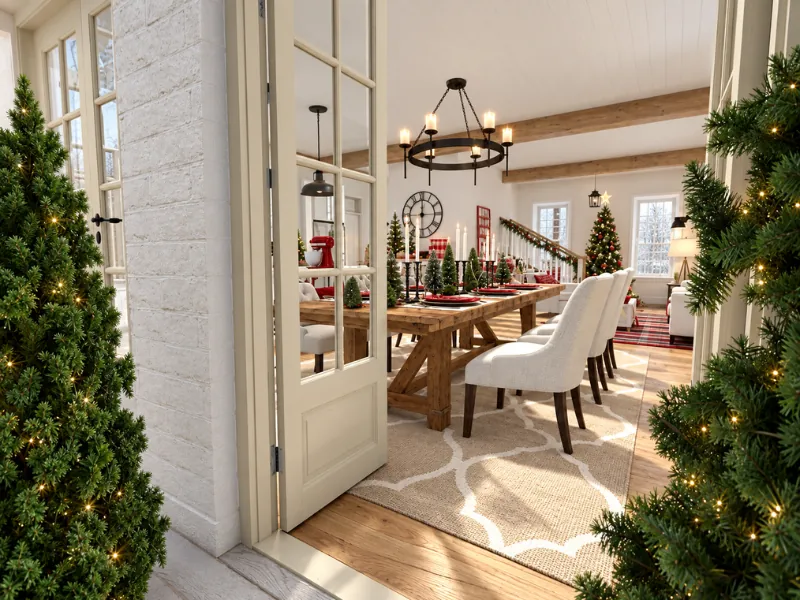 Christmas dining table set with red candles, greenery, miniature trees, and festive place settings.