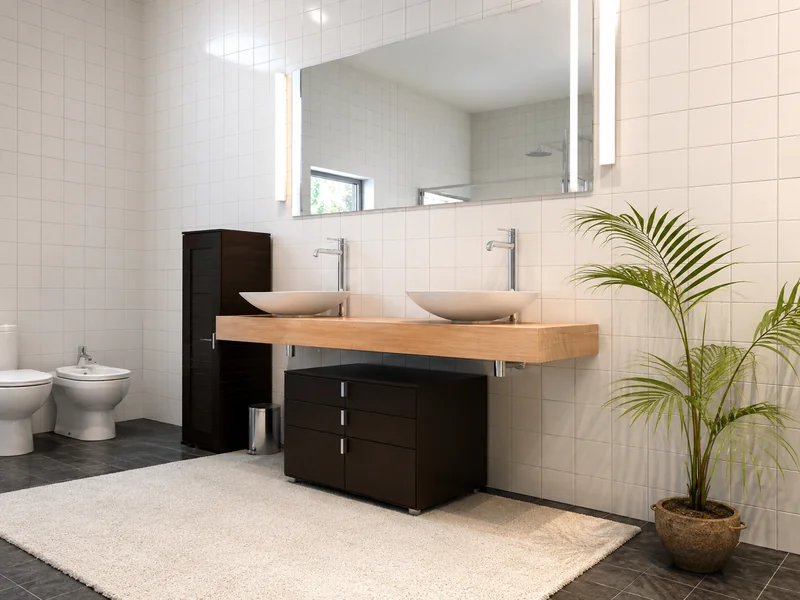 Photorealistic modern bathroom with white tiled walls, dark gray flooring, a floating light-wood vanity with two vessel sinks, dark cabinetry, a large mirror, and a potted palm beside a cream rug.