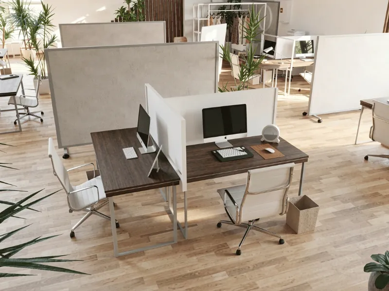 Modern open-plan office with paired wooden desks, desktop computers, white chairs, privacy partitions, light wood flooring, and potted plants.