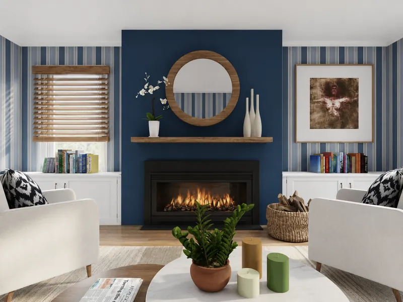 Cozy living room with a lit fireplace on a navy accent wall, striped wallpaper, round mirror, white armchairs, built-in shelving, plants, and candles.