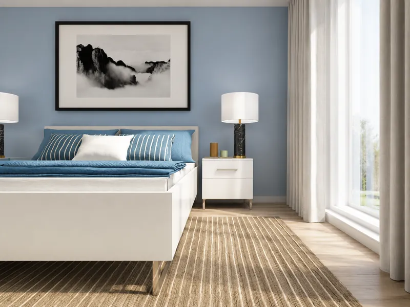 Bright blue-and-white bedroom with a white bed, striped blue bedding, matching nightstands and lamps, black-and-white wall art, and floor-to-ceiling windows.