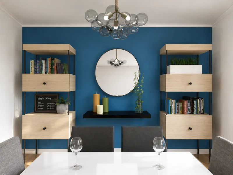 Modern dining area with a blue accent wall, round mirror, symmetrical wood-and-black shelving, floating console, candles, books, plants, and a glass globe chandelier.