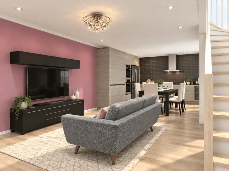Small open-plan living room with a gray sofa, wall-mounted TV, dining area, and kitchen beyond.