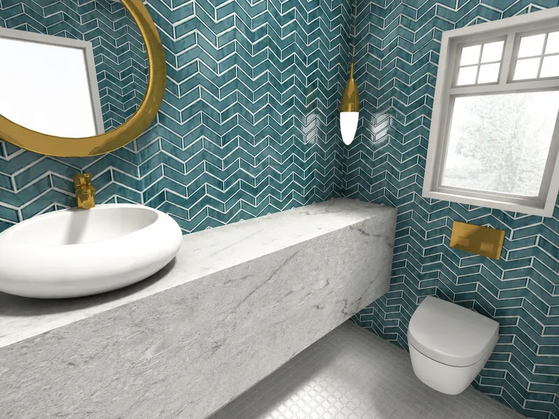 Compact powder room with glossy teal chevron wall tiles, a floating gray stone vanity, white vessel sink, round gold-framed mirror, brass fixtures, pendant light, and wall-mounted toilet beneath a window.