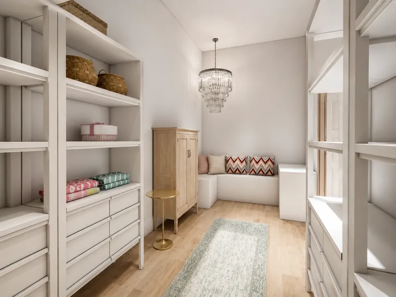 narrow dressing room with white built-in shelving and drawers, woven storage baskets, folded linens, a light wood cabinet, a small gold side table, a crystal pendant light, and a cushioned bench at the far end.