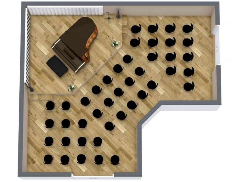 3D floor plan of a small concert hall featuring a grand piano on a raised stage and rows of black chairs arranged in angled sections facing the performance area. The room has wooden herringbone flooring and neutral-colored walls.