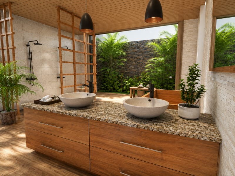 Tropical contemporary bathroom with a large wooden double vanity, stone vessel sinks, granite countertop, black pendant lights, open showers, wood ceiling, and lush garden views.