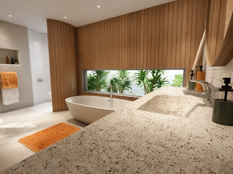 Modern bathroom with a terrazzo double sink vanity, freestanding tub, vertical wood-paneled walls, a wide garden-view window, and warm orange accents.
