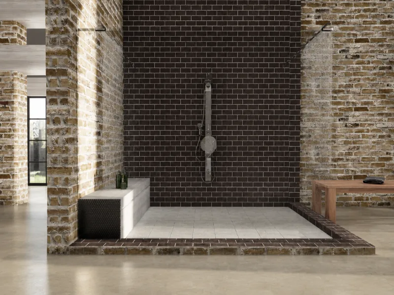 Open industrial wet room with exposed brick walls, black subway tiles, a walk-in shower, built-in bench, and polished concrete flooring.