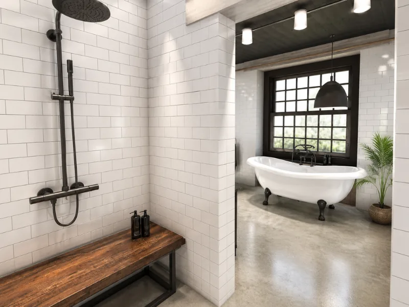 Industrial-style bathroom with white subway tiles, a black rainfall shower, rustic wood bench, polished concrete flooring, and a white clawfoot tub by a grid window.