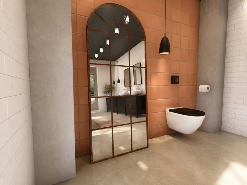 Industrial bathroom with a tall arched grid mirror, terracotta wall tiles, concrete surfaces, black pendant lighting, and a wall-mounted toilet.