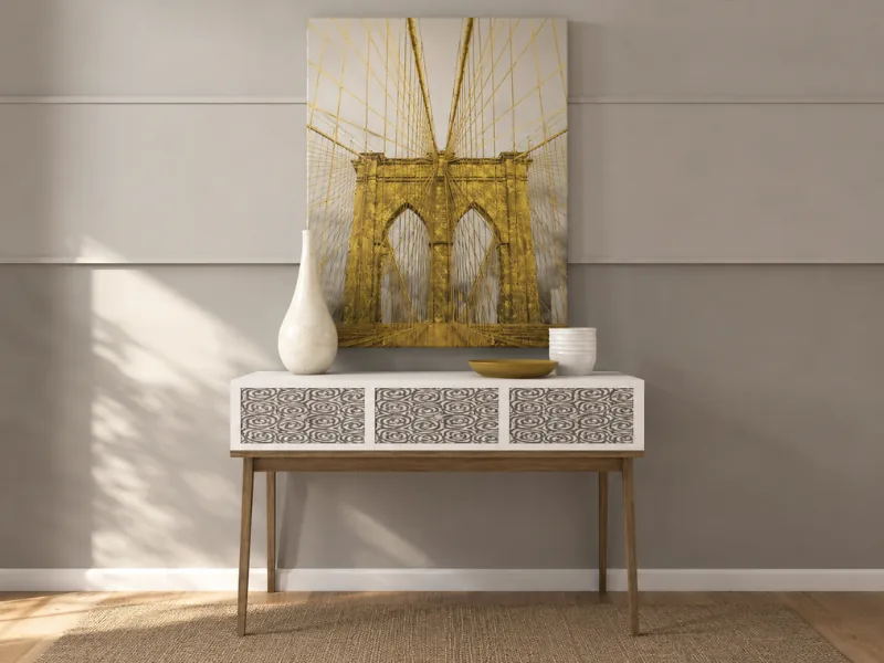 Modern console table with patterned drawer fronts, slim wood legs, neutral ceramics, and large golden bridge artwork against a taupe paneled wall.