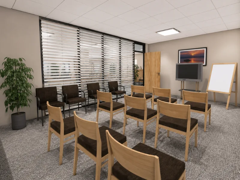 Dunder Mifflin’s conference room with rows of chairs, a television on a stand, whiteboard easel, large windows with blinds, and a potted plant.