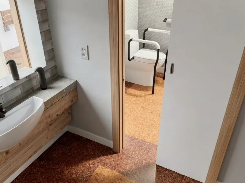 Accessible bathroom with a sliding door, wall-mounted sink, and support rails around the toilet to improve access and ease of use.