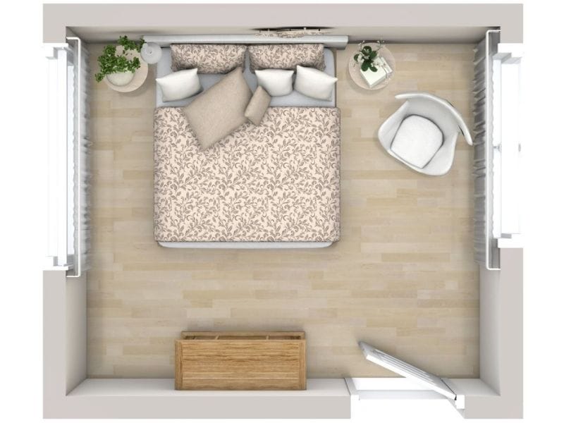 3D floor plan of a small bedroom with a double bed placed against the top wall, decorated with patterned bedding and multiple pillows. The room features light wood flooring, a wooden chest at the foot of the bed, a white armchair with a round side table on the right, and plants near the windows on both sides.