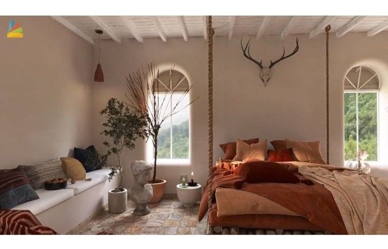 3D photo made with Homestyler. The photo is of a desert themed bedroom. The walls are white. The windows are long. The bed is hanging from ropes from the ceiling. There are warm earth tones of red as the bedding. Next to the bed is multiple items such as a tree in a pot, a large green plant, some candles on a night stand and a long bench with white cushions and multi-colored pillows. Stone flooring.