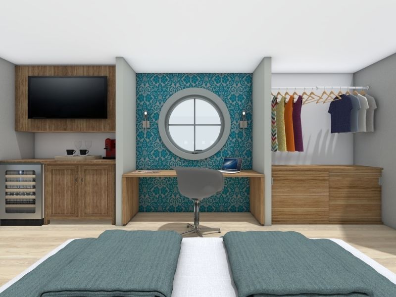 Modern hotel room with a bed in the foreground facing a work desk beneath a round window with patterned blue accent wall.