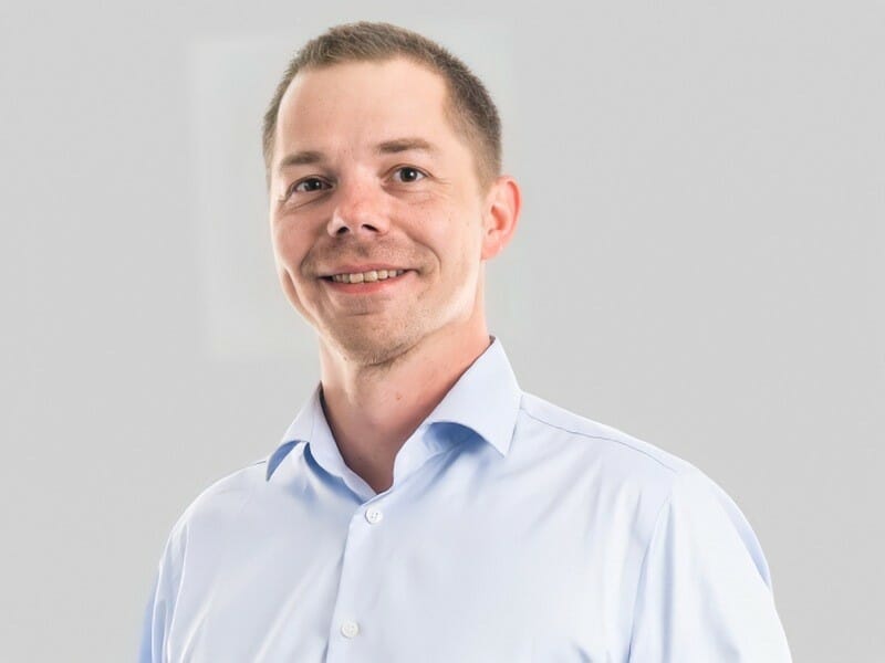 Der Bauunternehmer Tommy Nyborg in einem hellblauen Hemd posiert vor einem schlichten hellgrauen Hintergrund.