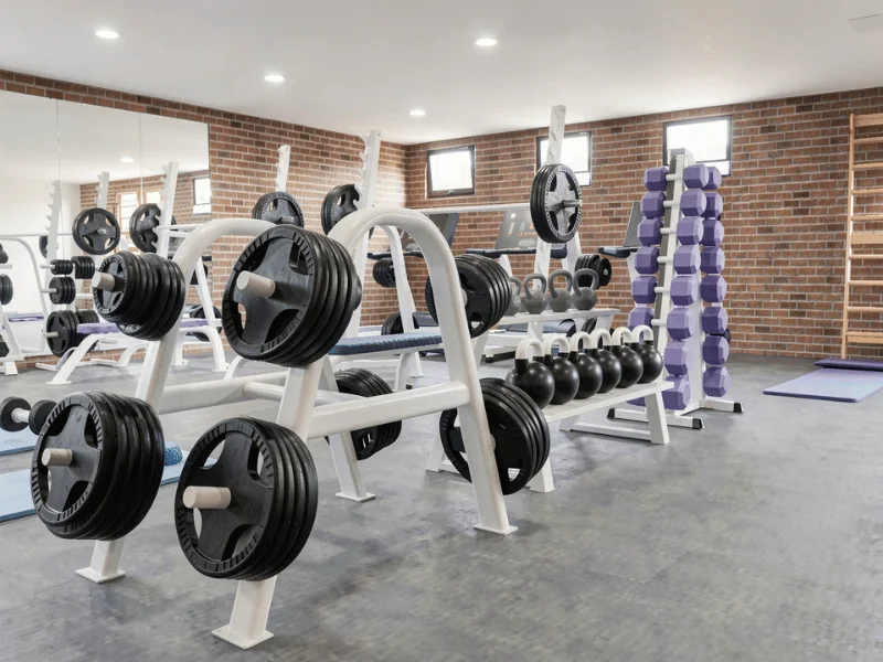 Fitness-Studio mit Hanteln, Gewichten, Kettlebells und Kraftgeräten vor Backsteinwänden und großen Spiegeln.