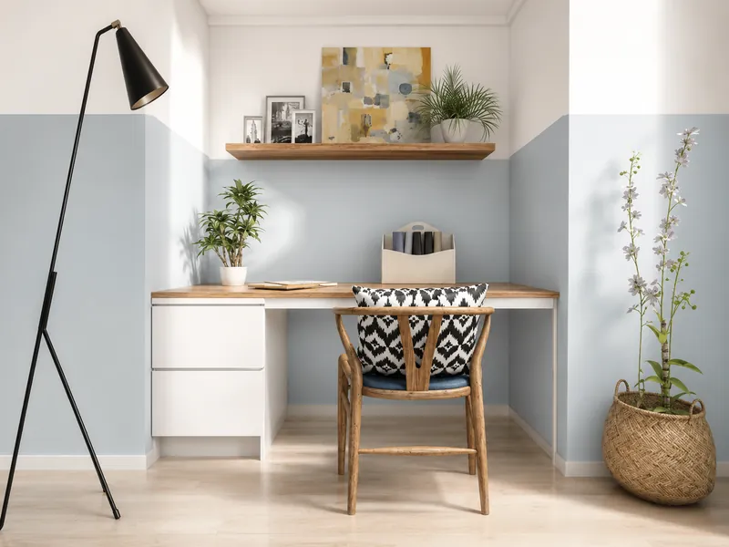 Kleines, helles Homeoffice mit integriertem Schreibtisch, Holzstuhl, Stehlampe, Pflanzen, Wandregal und dezenten hellblauen Wänden.